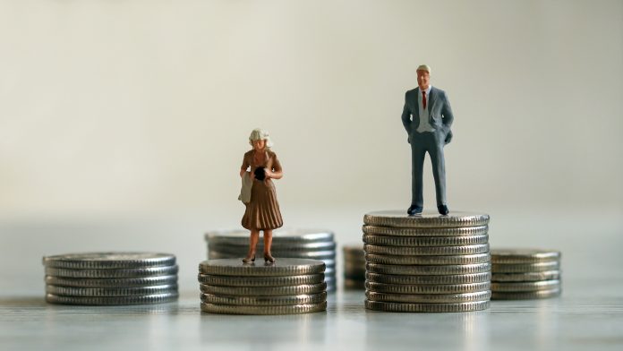 A miniature man and miniature woman standing on top of a pile of coins. The concept of the gender pay gap