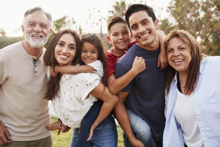 Three generation Hispanic family standing in the park, smiling to camera