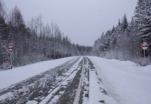 Road covered in snow and ice and lined by forest