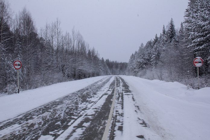 Road covered in snow and ice and lined by forest