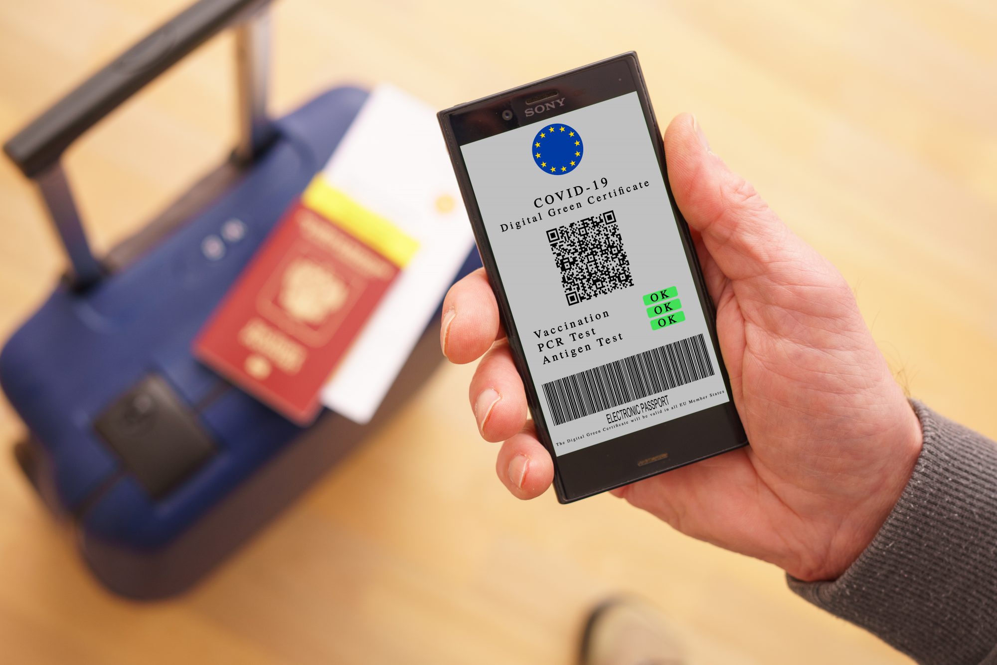 Mobile phone in hand with digital green certificate of vaccination covid-19. Phone screen with information about the presence of vaccinations and antibodies to covid against the background of a suitcase, passport and flight ticket