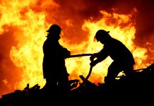 Silhouette of two firemen fighting a raging fire with huge flames of burning scrap timber