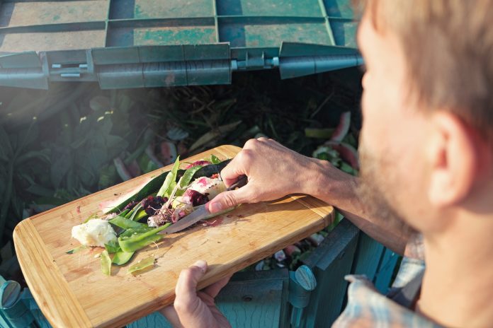 Person throws kitchen food waste into compost heap to make organic fertilizer. Composting - eco-friendly recycling technology