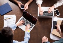 Young businesspeople sitting together at workplace and using digital devices