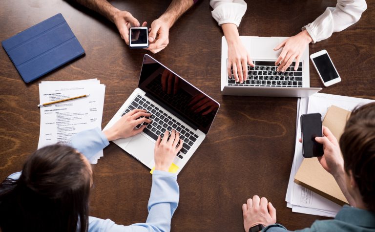 Young businesspeople sitting together at workplace and using digital devices