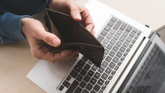 Man holding an empty wallet over computer because he lost his money to a fraudster