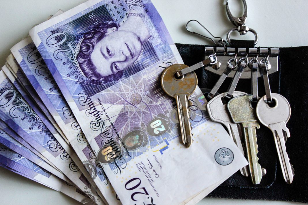 English twenty pounds cash money are liyng on a table with house keys in a black leather keyholder. Great Britain pounds. House payment, saving money to buy a house or to make a monthly payment for rent