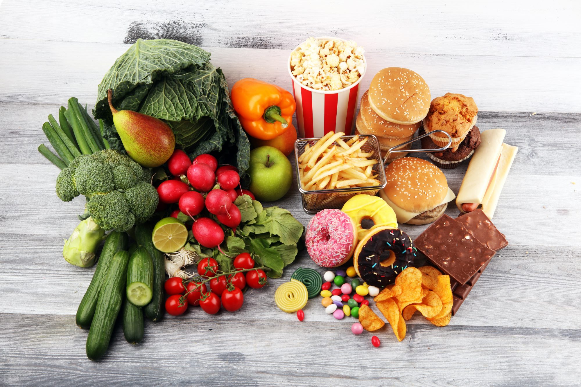 Healthy or unhealthy food. Concept photo of healthy and unhealthy food. Fruits and vegetables vs donuts,sweets and burgers on table