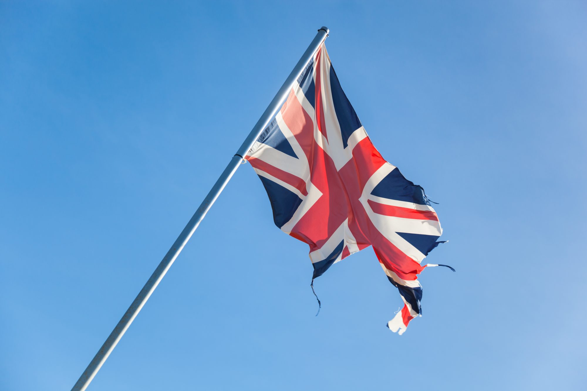 Tattered british flag in front of the blue sky. Concept for separatism or collapse of Great Britain