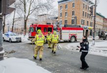 Firemen using broom to clean street corner from debris after car accident during winter day in Quebec city. Fire truck behind and police officer passing by