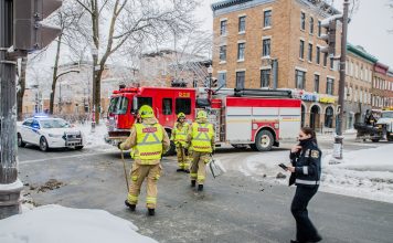 Firemen using broom to clean street corner from debris after car accident during winter day in Quebec city. Fire truck behind and police officer passing by
