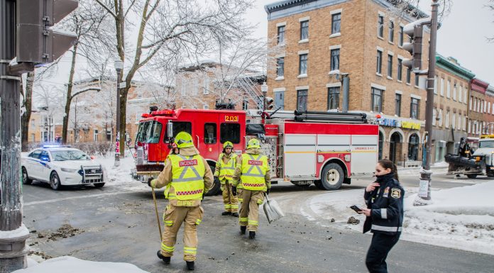 Firemen using broom to clean street corner from debris after car accident during winter day in Quebec city. Fire truck behind and police officer passing by