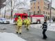 Firemen using broom to clean street corner from debris after car accident during winter day in Quebec city. Fire truck behind and police officer passing by