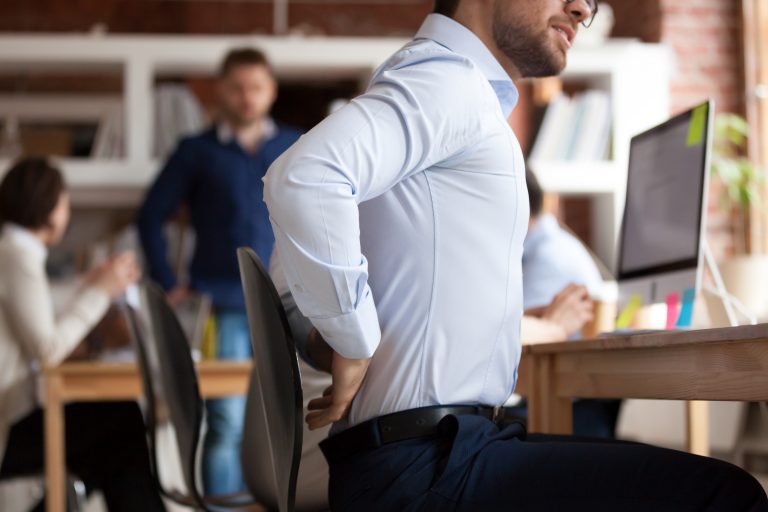 Businessman working sitting at desk feels unhealthy suffers from lower back pain. Damage of intervertebral discs, spinal joints, compression of nerve roots caused by wrong posture and sedentary work