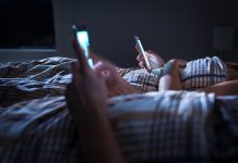 Bored distant couple ignoring each other lying in bed at night while using mobile phones. Smartphone addict. Obsessed and distracted man and woman texting. Addiction to social media and technology.