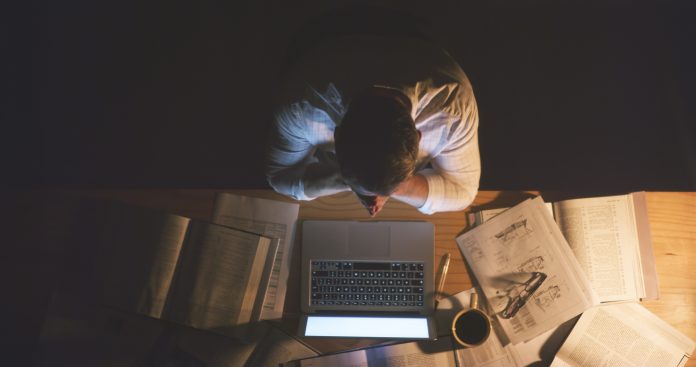 High angle shot of an unrecognizable businessman sitting alone in the office and feeling stressed while working a late night, an illustration of occupational stress