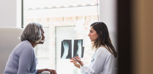 A serious female orthopedic doctor shows a senior female patient an x-ray of the patient's fractured foot.