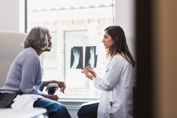 A serious female orthopedic doctor shows a senior female patient an x-ray of the patient's fractured foot.