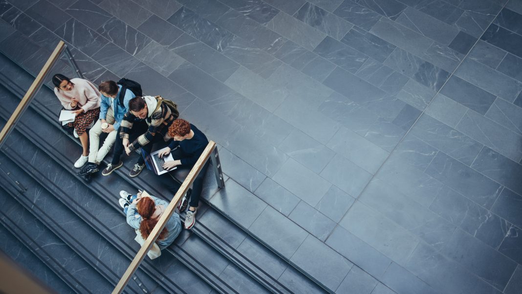 High angle view of university students sitting on stairs and discussing studies. Young people studying in college campus.