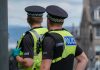 20th June 2020: Rear view of two male Police Scotland officers on duty in Edinburgh, during a Black Lives Matter demonstration in St Andrew Square, during the Coronavirus pandemic. One officer is wearing protective rubber gloves. Both officers are wearing high visibility jackets with their police uniforms, with the police logo on the back. They are standing looking down the street, keeping surveillance of the crowds. They have handheld radios attached to their jackets to communicate with colleagues.