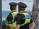 20th June 2020: Rear view of two male Police Scotland officers on duty in Edinburgh, during a Black Lives Matter demonstration in St Andrew Square, during the Coronavirus pandemic. One officer is wearing protective rubber gloves. Both officers are wearing high visibility jackets with their police uniforms, with the police logo on the back. They are standing looking down the street, keeping surveillance of the crowds. They have handheld radios attached to their jackets to communicate with colleagues.