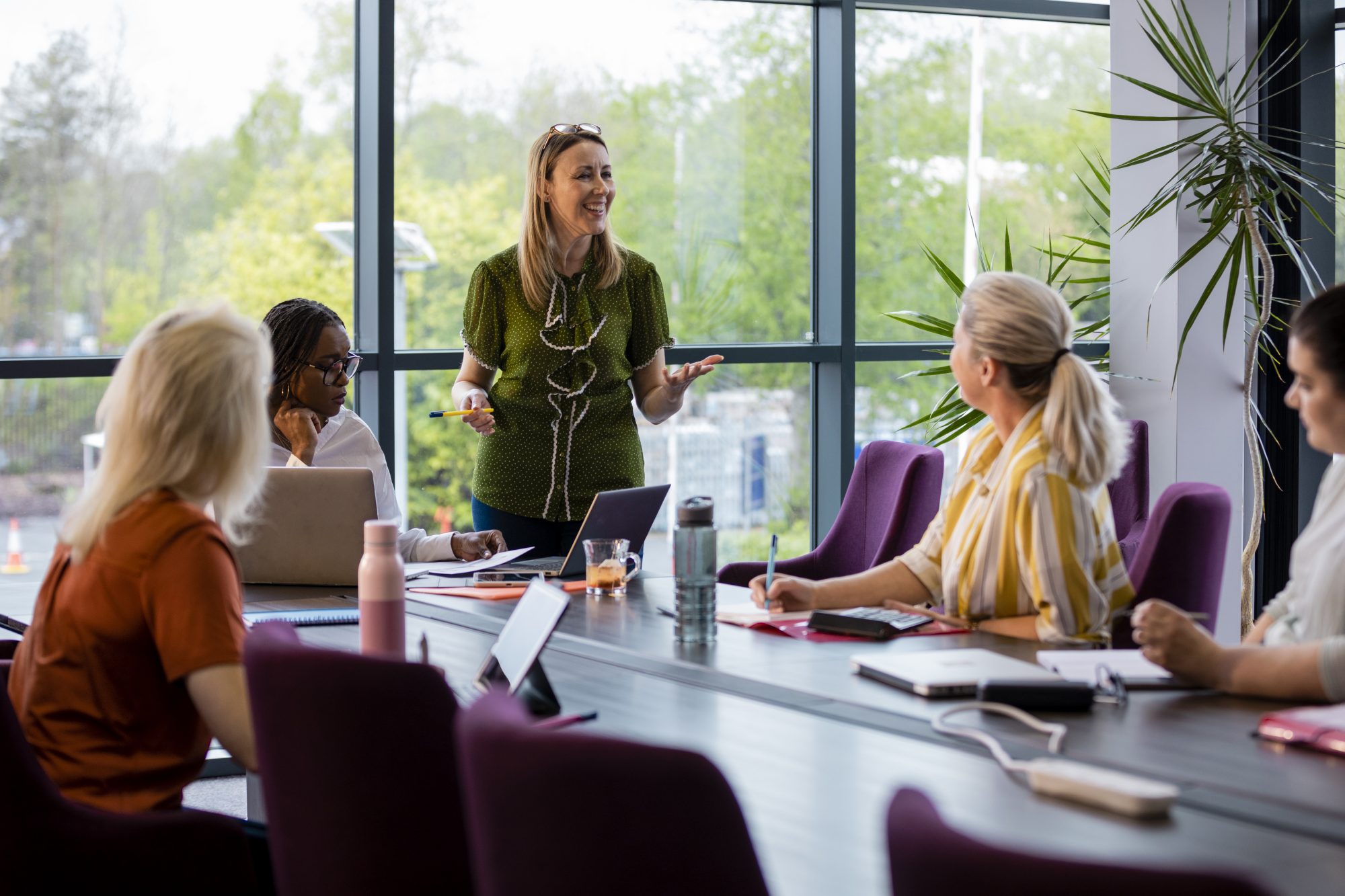 A wide angle view of a group of women gathering for a business meeting at their workplace in Hexham.  The woman in the green blouse leads the meeting and encourages the others to participate.