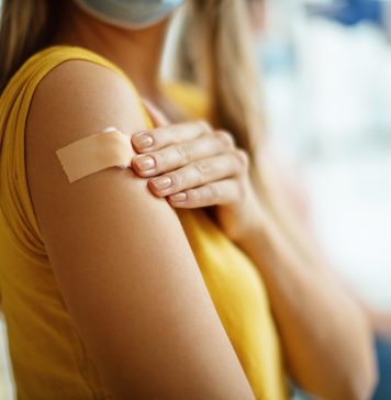 Doctor had just vaccinated a young unrecognizable female patient in the hospital. She is pleased with how it all went. Focus on adhesive bandage.