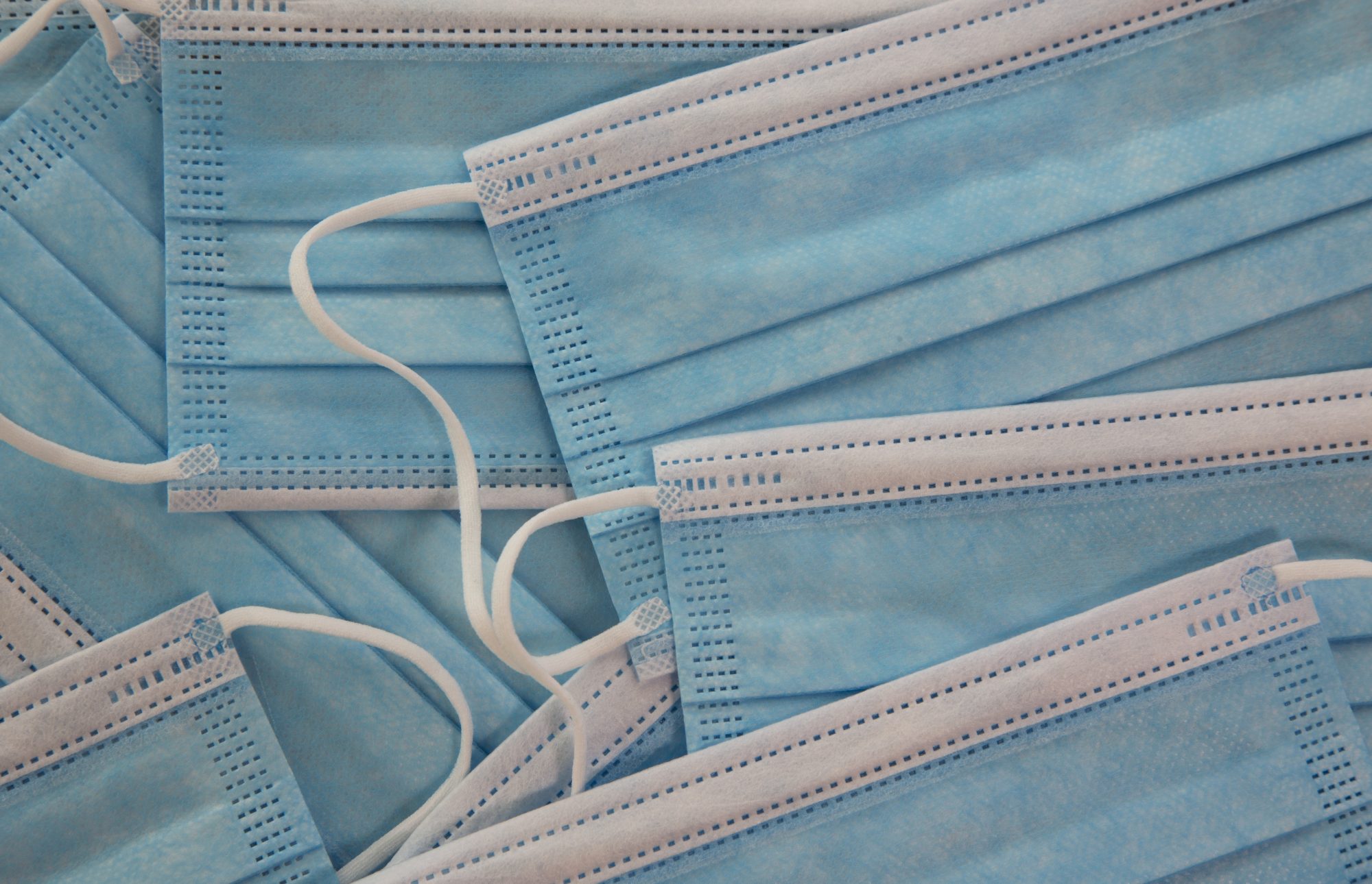 Background of close up of multiple, light blue and white medical masks, protection against infectious disease