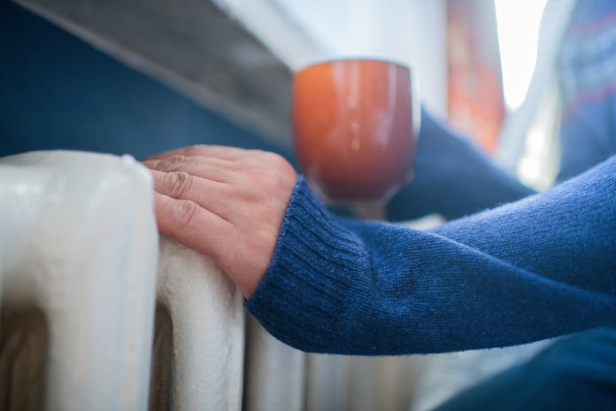 Man in warm sweater with hot tea near radiator in winter. Energy crisis concept.