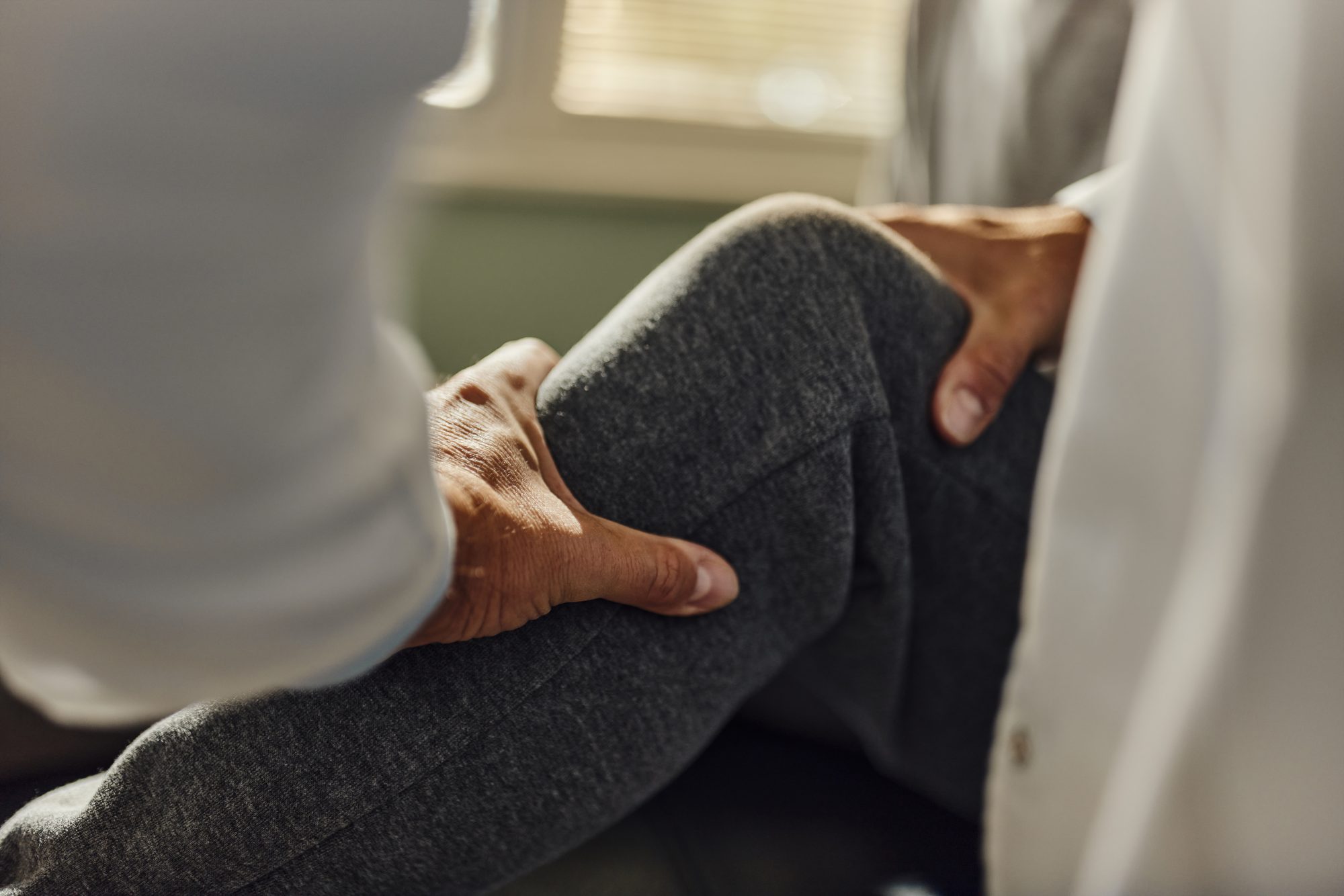 Close up of unrecognizable doctor examining patient's knee during an appointment in the office.