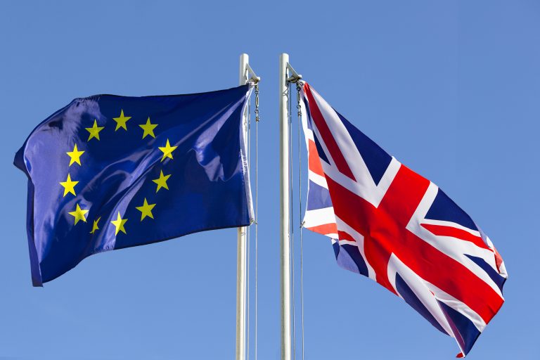 European Union flag and flag of UK on flagpole in front of blue sky