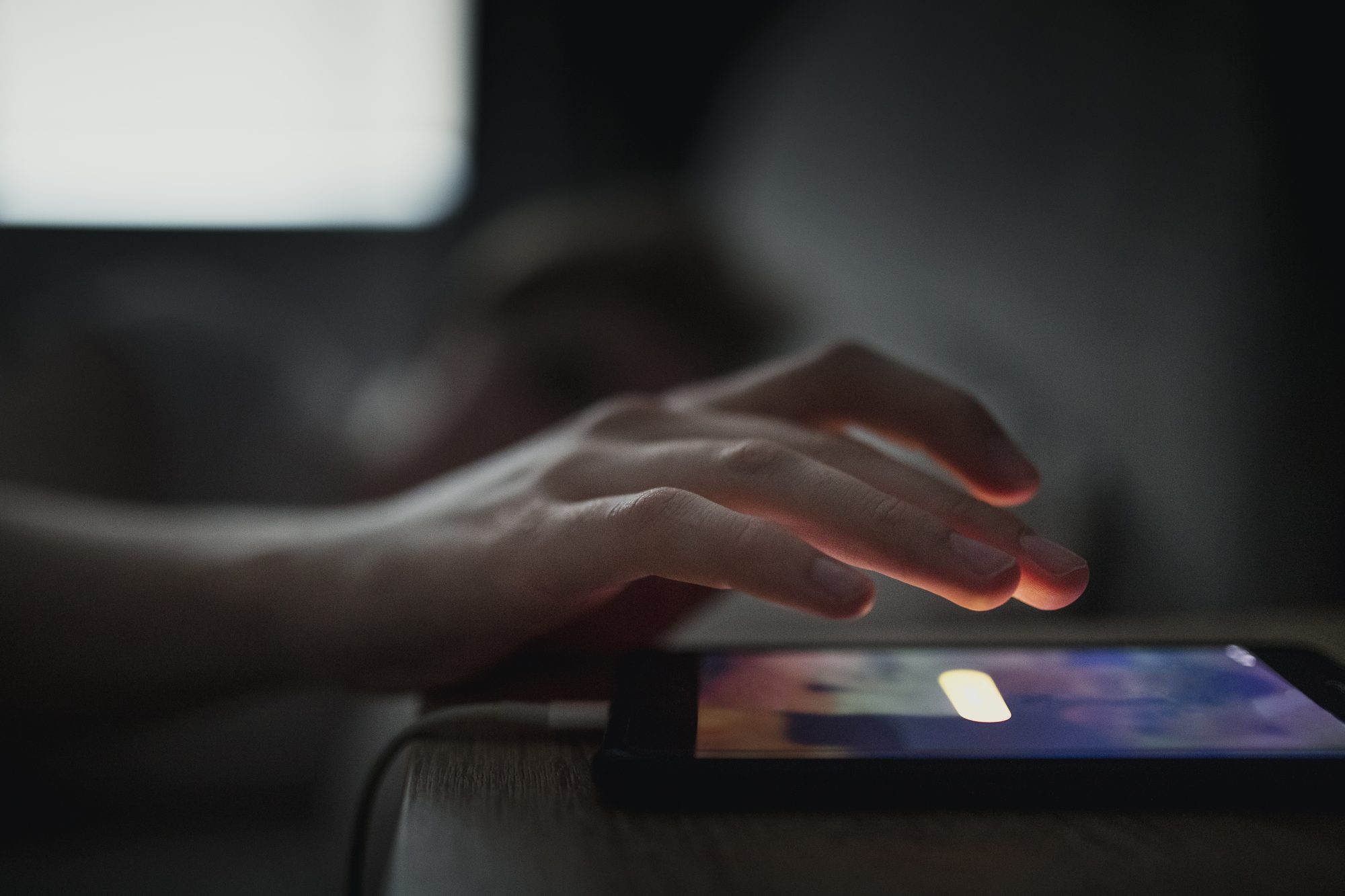 Unrecognisable male going to touch the snooze button on his mobile phone. The alarm is waking him up in the morning.