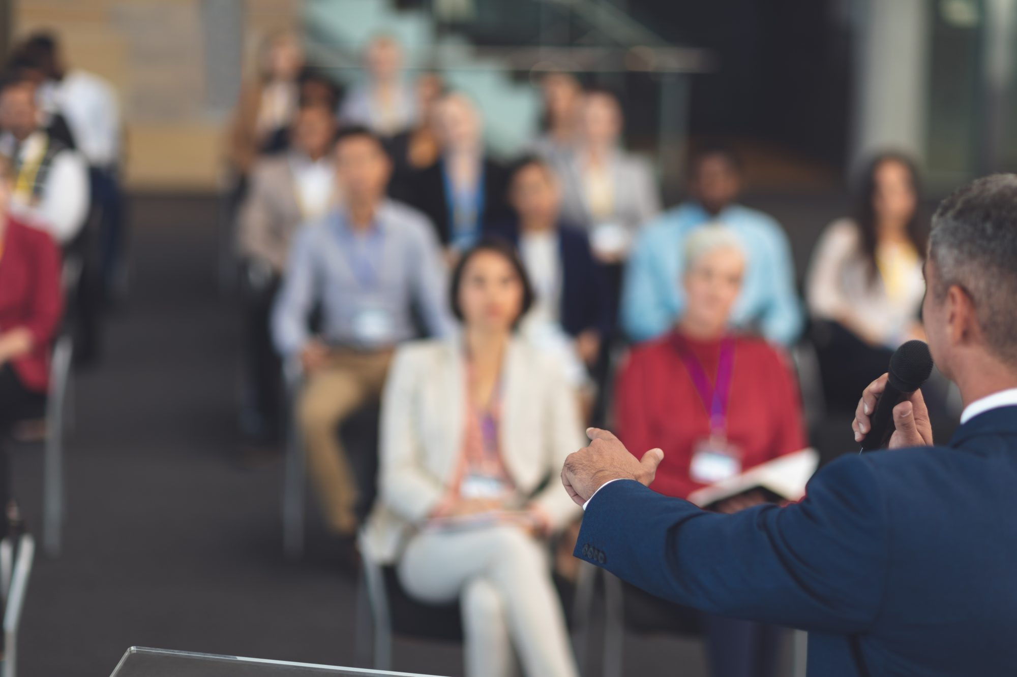 Rear view of mixed race businessman holding microphone while speaking at a business seminar in modern office building