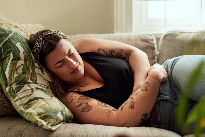 Shot of a young woman suffering from stomach cramps on the sofa at home