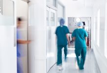 Motion Blur Shot Of Medical Staff Wearing Scrubs In Busy Hospital Corridor