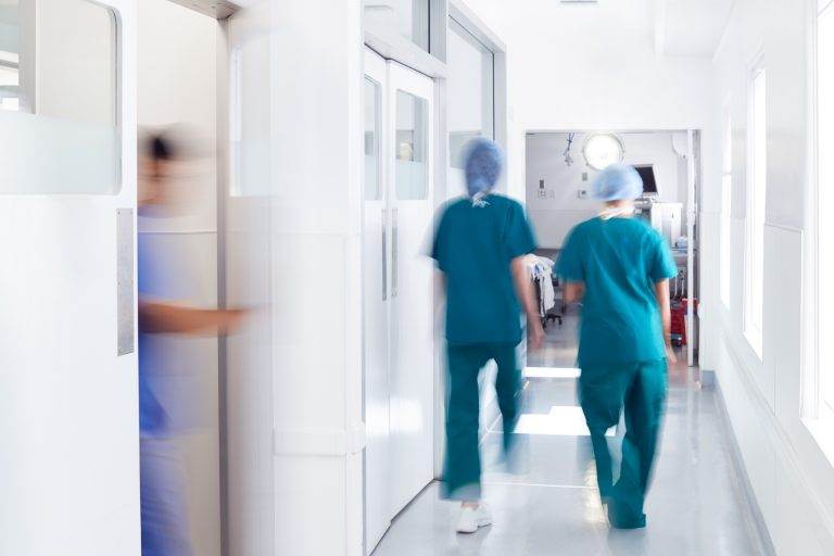 Motion Blur Shot Of Medical Staff Wearing Scrubs In Busy Hospital Corridor