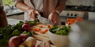 Female hands cutting vegetables on cuttiing board - woman preparing a healthy meal to boost the immune system