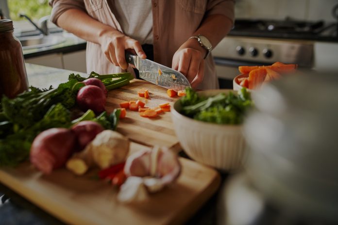 Female hands cutting vegetables on cuttiing board - woman preparing a healthy meal to boost the immune system