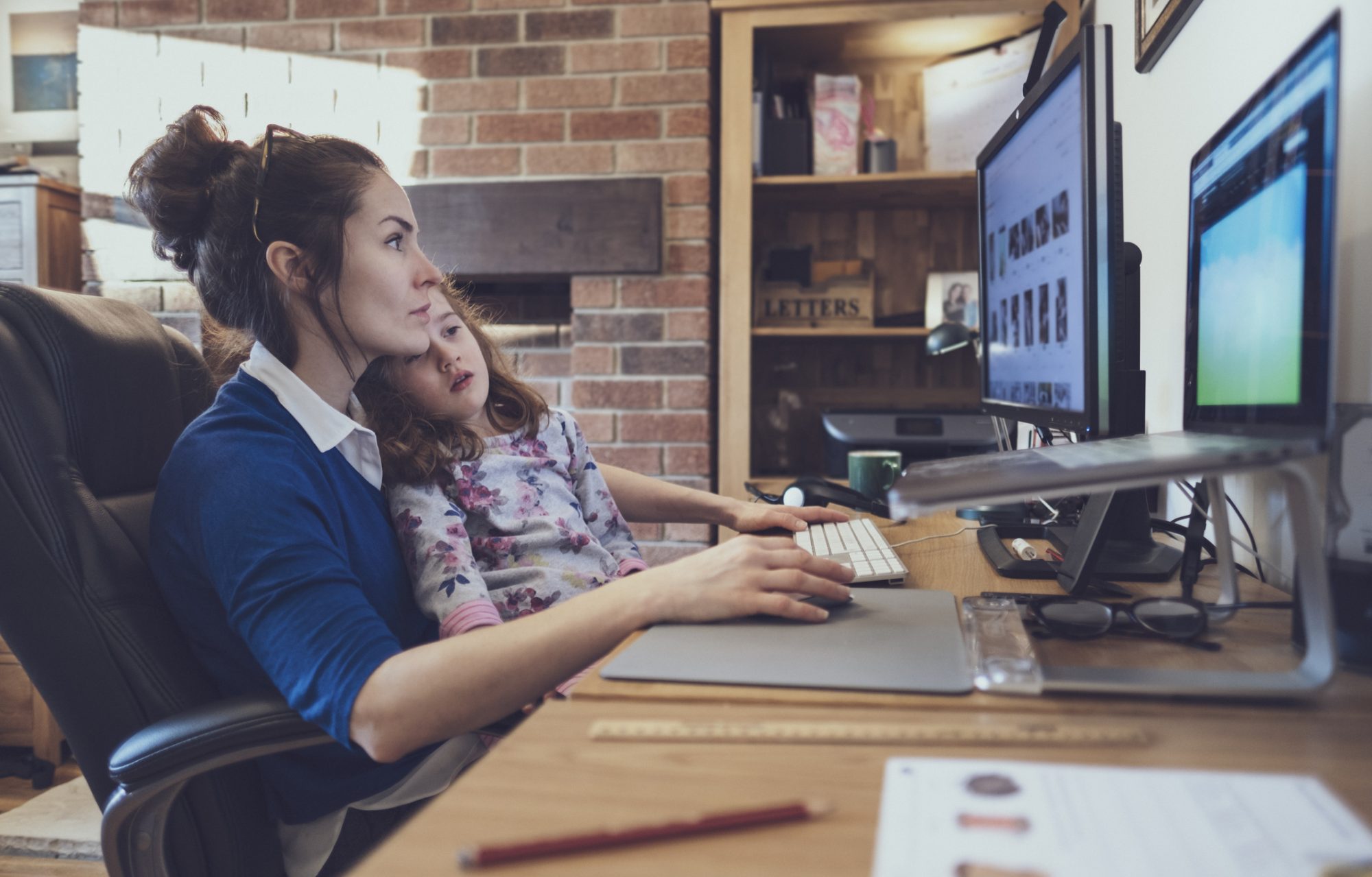 A woman is working from her home office while attempting to home school her daughter.