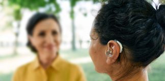 Adult woman with a hearing impairment uses a hearing aid to communicate with her female friend at city park. Hearing solutions, sensorineural hearing loss