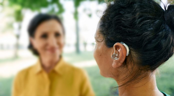 Adult woman with a hearing impairment uses a hearing aid to communicate with her female friend at city park. Hearing solutions, sensorineural hearing loss