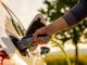 Hand of man inserting a power cord into an electric car for charging ecofriendly vehicle on green landscape