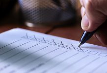 Close up image of a person’s hand using a ballpoint pen to put a check or tick mark in a row of boxes on a paper form sheet.