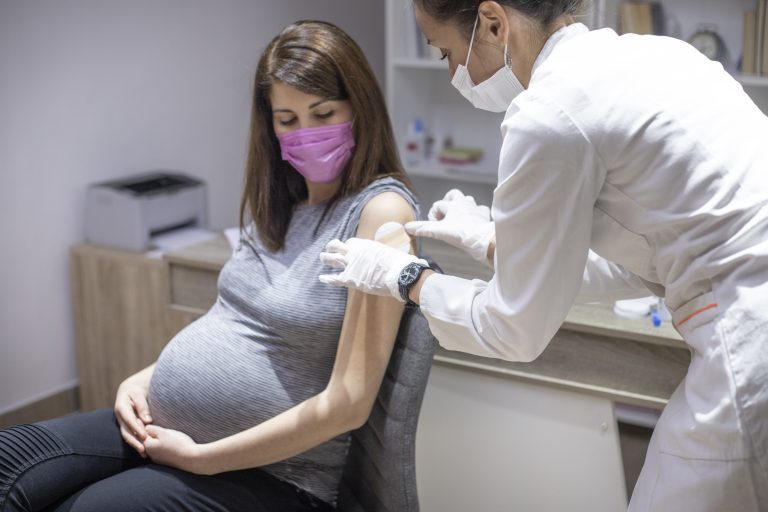 Pregnant woman taking a vaccination against covid-19 virus during pandemic in medical clinic office.