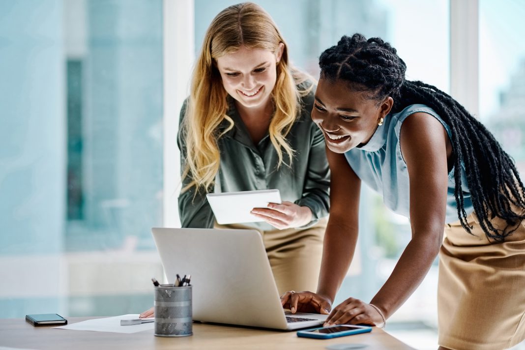 Two diverse businesswomen working together on a digital tablet and laptop in an office