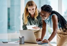 Two diverse businesswomen working together on a digital tablet and laptop in an office