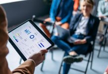 Close up photo of man hand holding tablet while group of business people listening to his analysis.