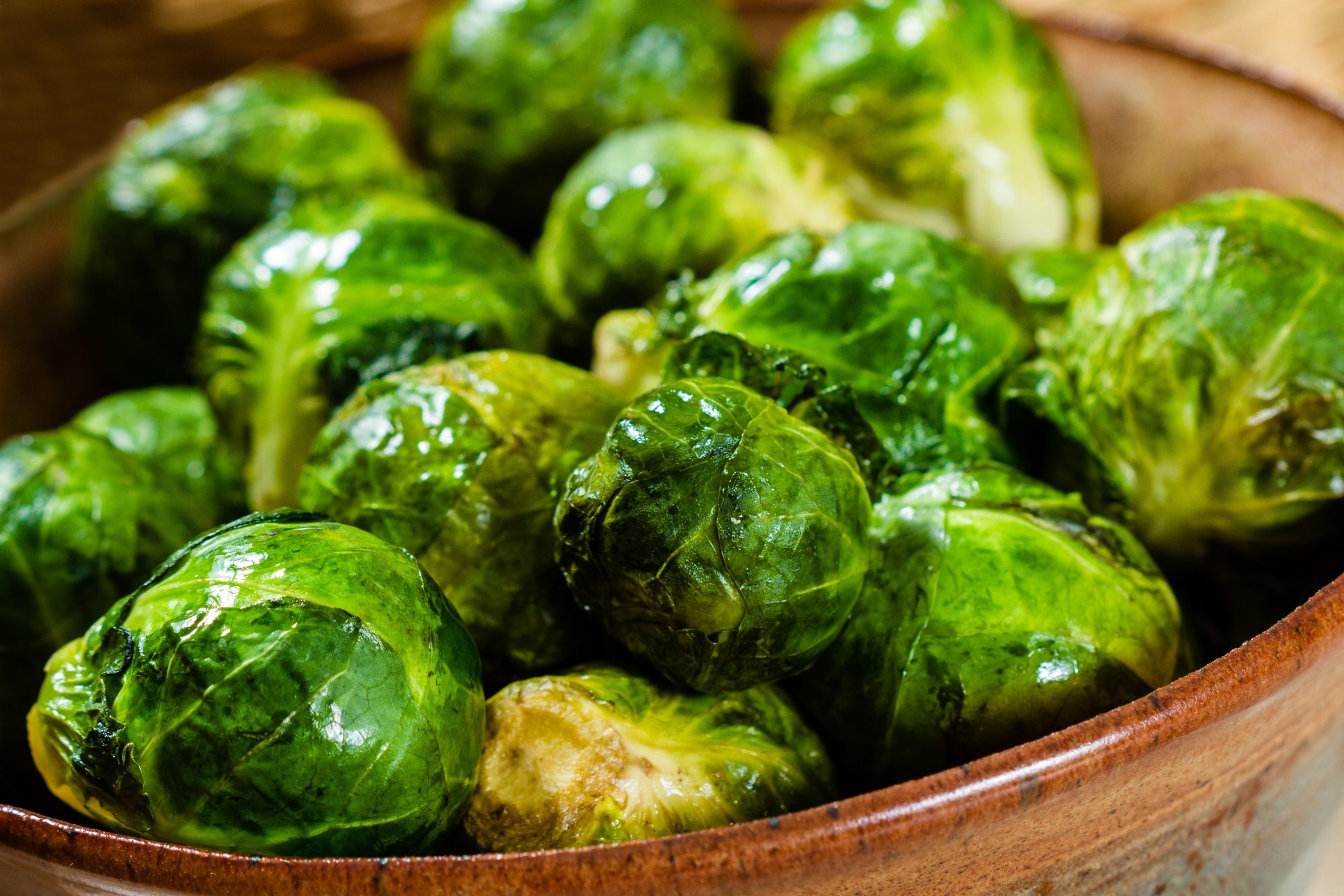 Freshly cooked, glistening Brussels Sprout in a pottery bowl.