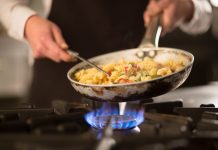 Female cook preparing pasta dish with vegetables on stove