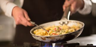 Female cook preparing pasta dish with vegetables on stove